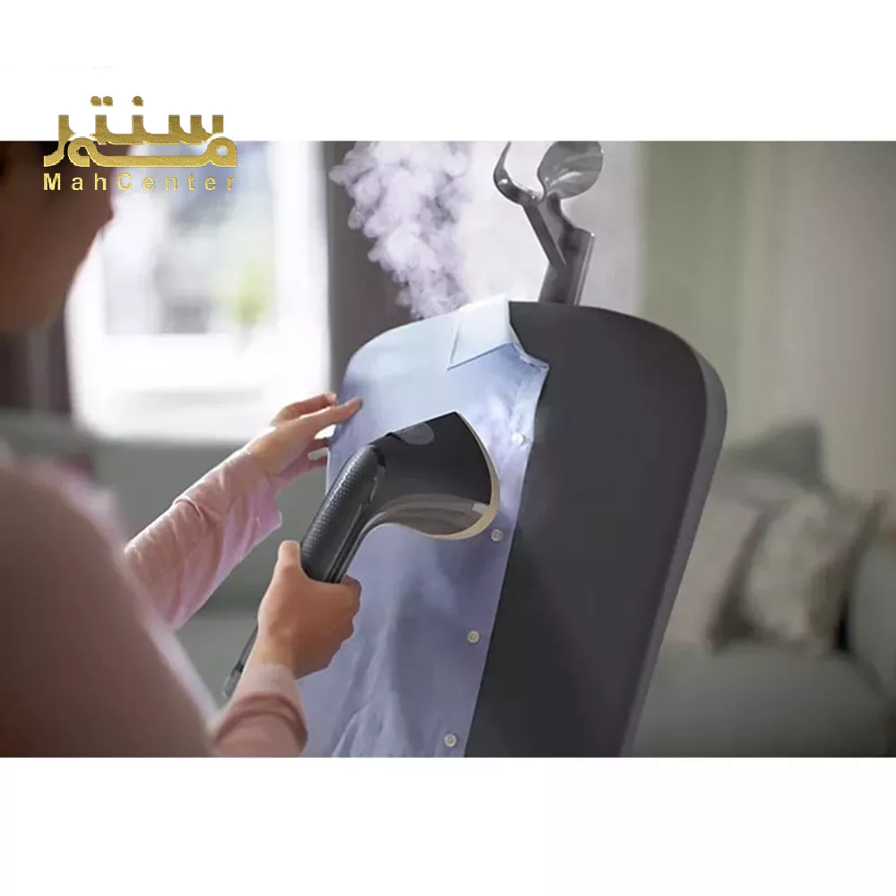 در تصویر، یک خانم در حال استفاده از دستگاه بخارگر برای صاف کردن چروک‌های یک پیراهن مردانه آبی رنگ دیده می‌شود.