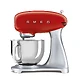 یک میکسر ایستاده SMEG SMF02 قرمز با یک کاسه و یک پیوست روی یک پس زمینه سفید.