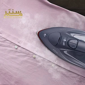 یک اتو بخار AEG روی یک پیراهن صورتی نشان داده شده است. اتو بخار خاکستری و مشکی است و در حال اتو کردن پیراهن است