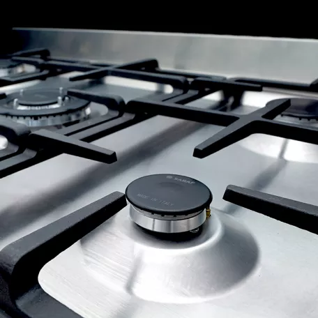 تصویر نزدیک از اجاق گاز با سطح استیل براق و شعله‌پخش‌کن‌های مدرن ساخت ایتالیا.