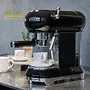 یک دستگاه اسپرسوساز مشکی Smeg ECF01 روی یک میز فلزی ضد زنگ نشسته است. دو فنجان قهوه در پس زمینه قرار دارند.