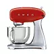 یک میکسر ایستاده SMEG SMF02 قرمز با یک کاسه و یک پیوست روی یک پس زمینه سفید.