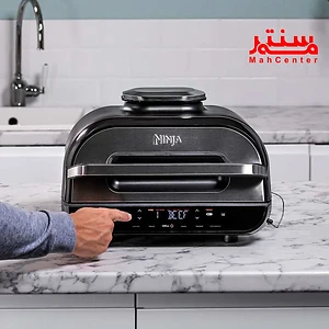 "یک دستگاه آشپزی نینجا مشکی با صفحه نمایش دیجیتال و تنظیمات، قرار گرفته روی میز سنگ مرمر در آشپزخانه."
