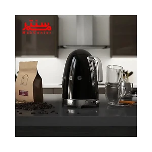 یک کتری مشکی SMEG در پس زمینه سفید نمایش داده می شود. کتری پر از آب است و روی پایه خود قرار دارد. دو فنجان چای در کنار کتری قرار دارند.